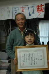 「蚕を通じて子供時代のことを思い出す」と話す山田さんと、入賞した「繭クラフト作品展」の賞状を手にする孫の要ちゃん