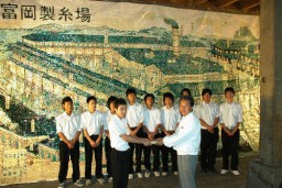 壁画が飾られた東繭倉庫内で岩井市長に寄付金を手渡す生徒たち