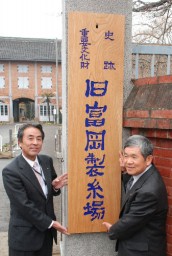 門柱に掲げた看板と須賀会長(左)