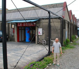 「のこぎり屋根工場を制作の場として活用し、その魅力を地域に伝えたい」と工房をバックに話す金原さん